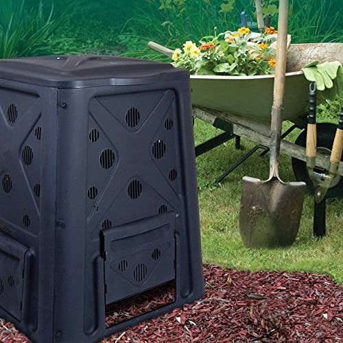 Compost bin with gardening tools and wheelbarrow in garden.