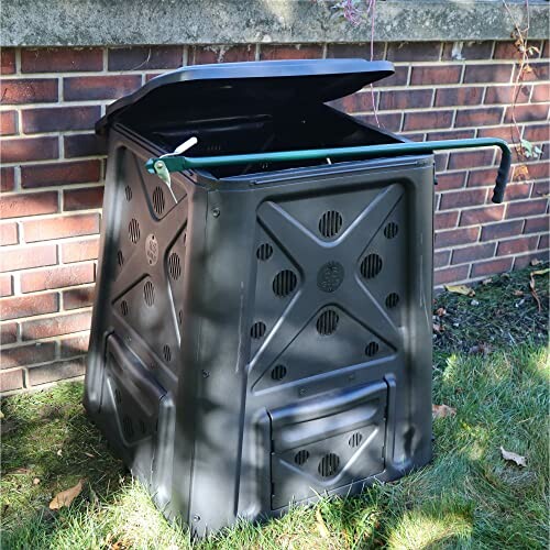 Outdoor compost bin with a lid against a brick wall.